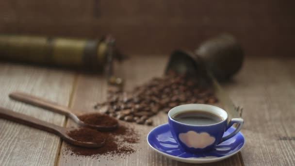 Coffee beans and ground coffee in wooden spoons on brown background. With coffee pot, blue coffee cup and coffee grinder. - Footage, Video