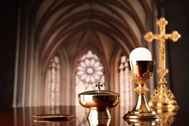Первое причастие. Тема католической религии. Распятие, крест и золотая чаша и вафля на алтаре в церкви. - Фото, изображение