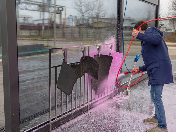Egy férfi rózsaszín habbal borítja az autószőnyegeket egy önkiszolgáló autómosóban. - Fotó, kép