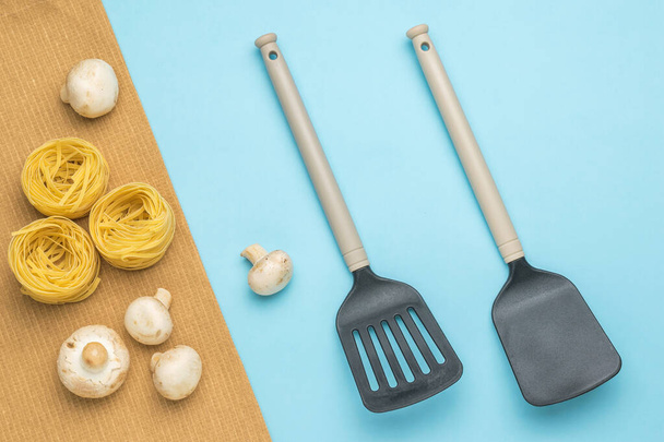 Pâtes, champignons et deux spatules de cuisine sur fond bleu. Ingrédients pour la fabrication de pâtes. - Photo, image