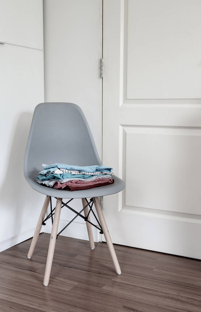 Stack of folded clean clothes on modern chair in the corner of bedroom. - Fotó, kép