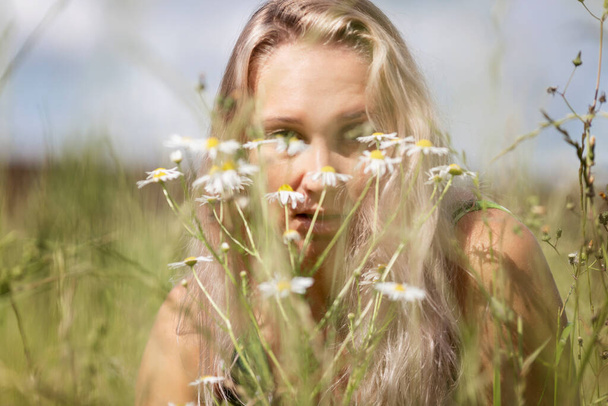 Young blond woman in a field with camomiles. Rest on a summer day. Close-up. - Fotó, kép