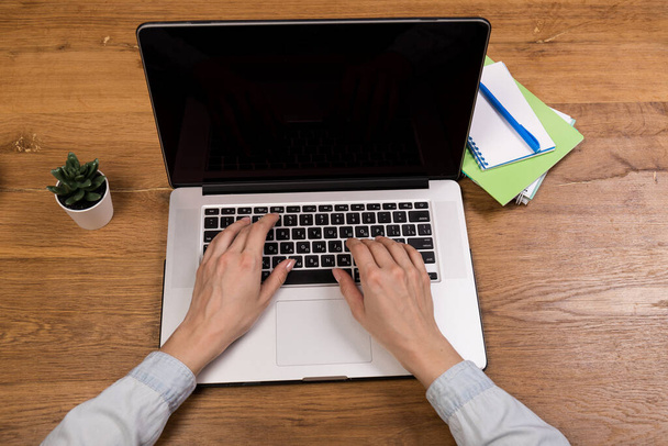 Een vrouw met een laptop op een oude houten tafel. Mix van kantoorbenodigdheden en gadgets op een houten bureauondergrond. kopieerruimte. - Foto, afbeelding