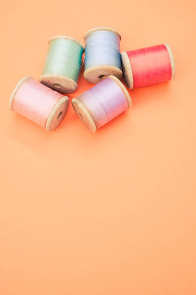 A colorful sewing threads isolated on a pastel orange background with free space for text - Fotoğraf, Görsel