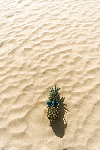 A funny photo of a pineapple with sunglasses lying on a sandy beach with space for your text - Fotoğraf, Görsel