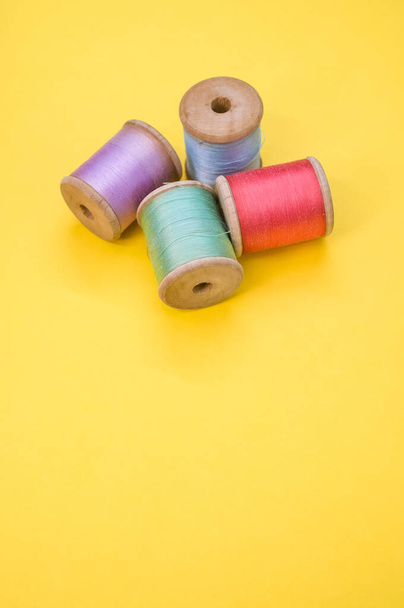 A colorful sewing threads isolated on a yellow background with free space for text - 写真・画像