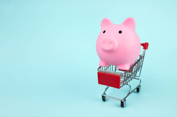 Koncepcja zakupów internetowych. Różowa świnka bank wewnątrz mini wózka supermarketu na niebieskim tle z miejsca do kopiowania. Koncepcja oszczędzania pieniędzy na zakupach. - Zdjęcie, obraz