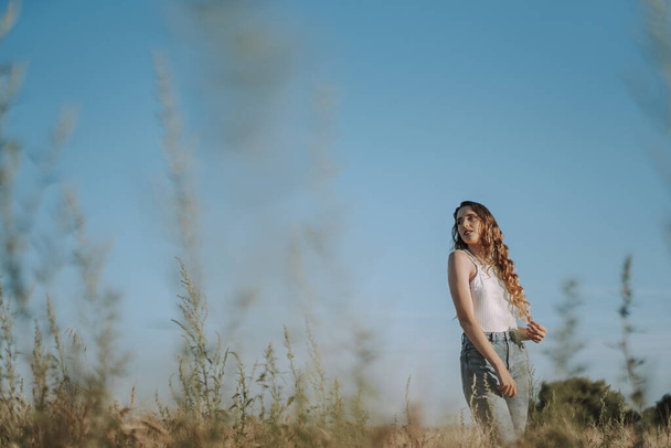 A Spanish girl pulling on her blond locks in a wheat field on a sunny day under a clear ksy - Φωτογραφία, εικόνα