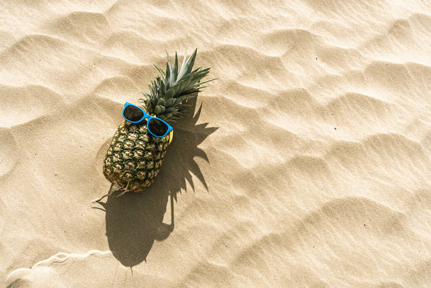 A funny photo of a pineapple with sunglasses lying on a sandy beach with space for your text - Fotografie, Obrázek