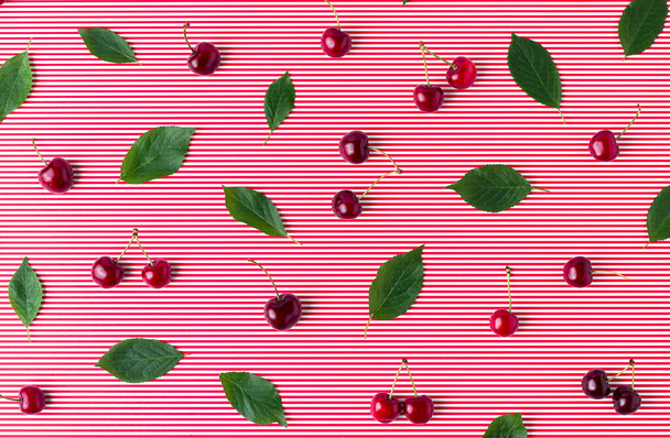 Concepto de verano con cerezas dulces y hojas verdes sobre fondo rojo despojado. plano laico vista superior fruta patrón. - Foto, imagen
