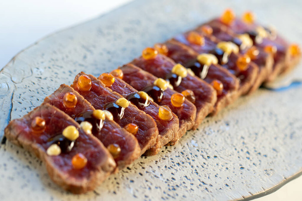 Macro close-up van smakelijke wagyu beef sirloin tataki. Meerdere schijfjes knapperig en roodachtig vlees georganiseerd op bord. - Foto, afbeelding