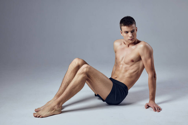чоловічий спортсмен надуває тіло, сидячи на підлозі позує модель
 - Фото, зображення