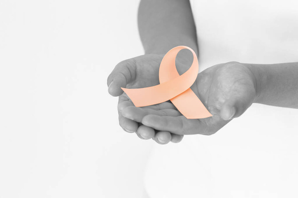 Hand holding Peach color ribbon curl on white fabric background with copy space, symbol for Uterine and Endometrial cancer awareness, World Cancer Day. Healthcare or hospital and insurance concept. - 写真・画像