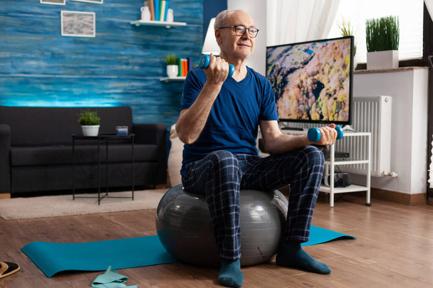 Hombre mayor sosteniendo pesas haciendo ejercicio de brazos estirando los músculos del cuerpo - Foto, Imagen