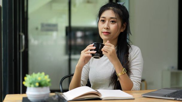 Portrait of female teenager take a break and drinking hot beverage while reading book at home - Photo, Image