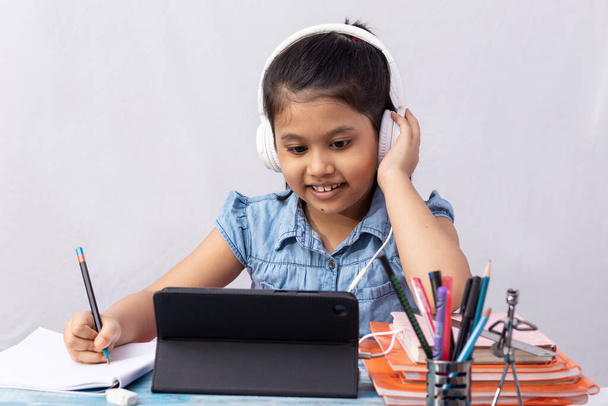 Ładna indyjska dziewczynka uczęszczająca na zajęcia online z tabletem i słuchawką na białym tle - Zdjęcie, obraz