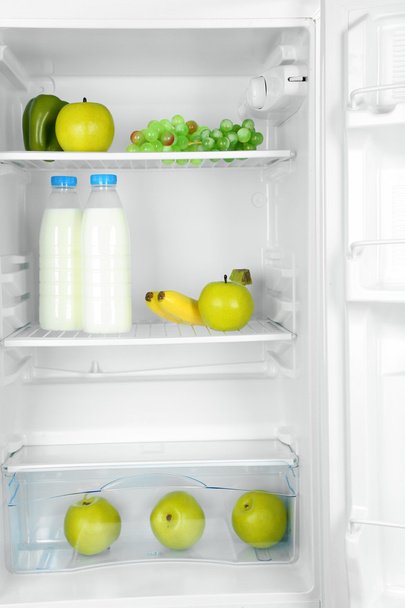 Milk bottles, vegetables and fruits in open refrigerator. Weight loss diet concept. - Photo, image