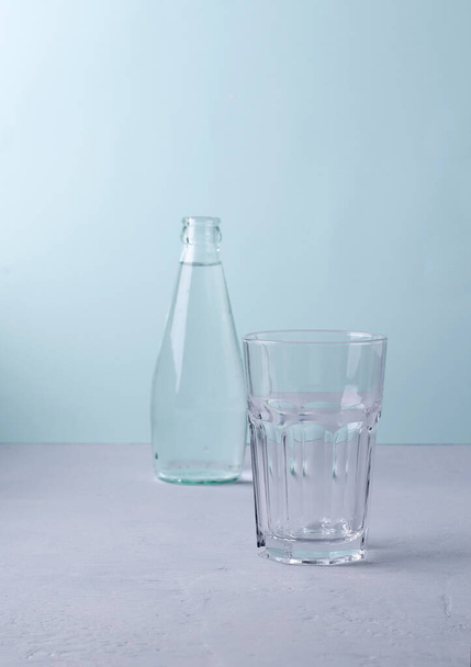 An empty glass on a blue background. Background blurred glass bottle, selective focus, copying space - Photo, Image