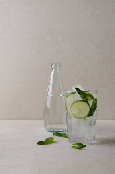 Холодный напиток с кусочками лайма, льда и мяты в стакане на бежевом фоне - Фото, изображение