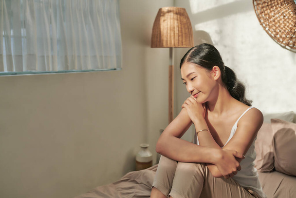 Cheerful happy asian girl in sleepwear smiling, sitting on bed at home. - Valokuva, kuva