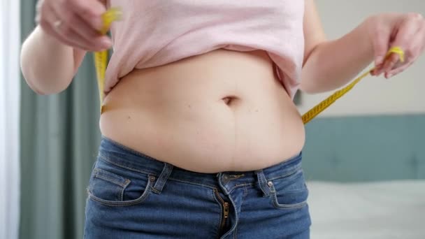 Νεαρή γυναίκα που μετράει μεγάλη κοιλιά με μεζούρα. Έννοια της δίαιτας, ανθυγιεινό τρόπο ζωής, υπέρβαρο και παχυσαρκία - Πλάνα, βίντεο