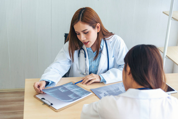 Two asian women doctors discuss meeting doctor's office medical clinic looking x-ray film consulting patient disease. Asian medical lab young women talking together discussing healthcare teamwork - Photo, Image