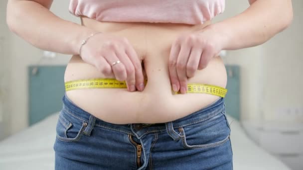 Jonge dikke vrouw met overgewicht die haar dikke buik meet met meetlint. Concept van dieet, ongezonde levensstijl, overgewicht en obesitas - Video