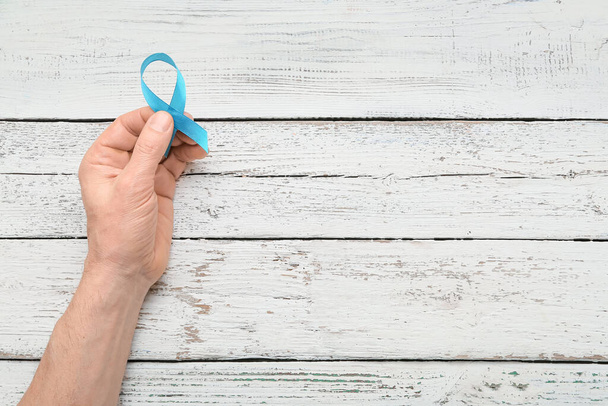Male hand with light blue ribbon on wooden background. Prostate cancer concept - Fotoğraf, Görsel