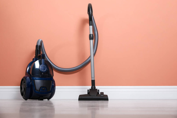 Modern vacuum cleaner on floor near orange wall indoors. Space for text - Photo, image