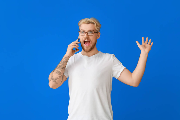 Surpreendido bonito homem falando por telefone celular no fundo de cor - Foto, Imagem