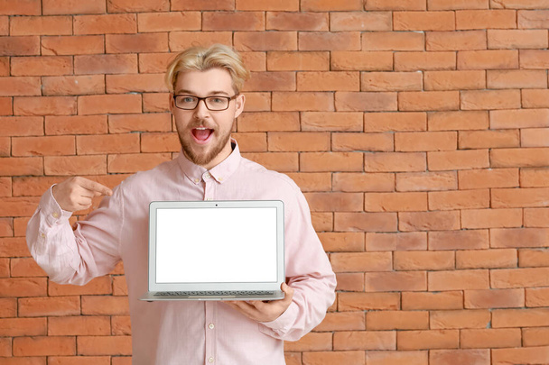 Handsome man pointing at laptop on brick background - Photo, Image