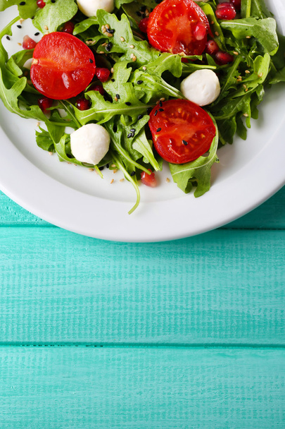 Green salad made with  arugula, tomatoes, cheese mozzarella balls and sesame  on plate, on color wooden background - Foto, Imagem