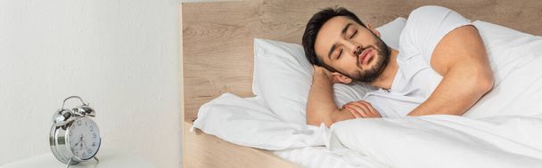 Young man sleeping near alarm clock in bedroom, banner  - Фото, зображення