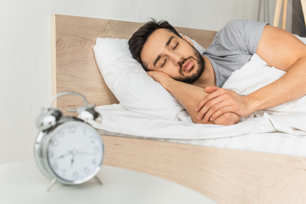 Young man sleeping near blurred alarm clock on bedside table  - Zdjęcie, obraz
