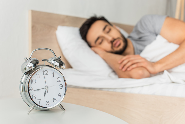 Alarm clock on table near blurred man sleeping on bed  - Valokuva, kuva