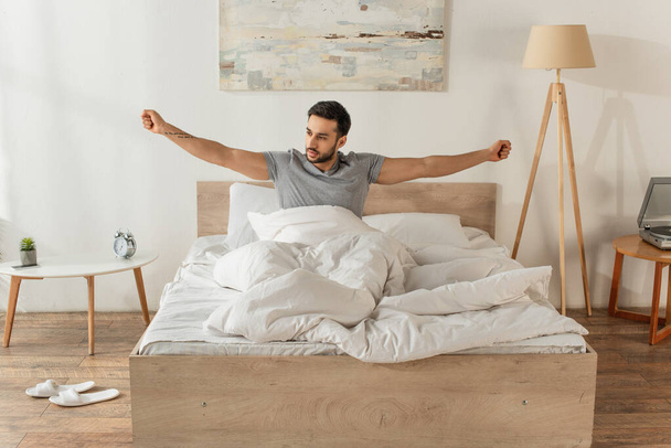 Bearded man stretching while sitting on bed in morning  - Fotoğraf, Görsel