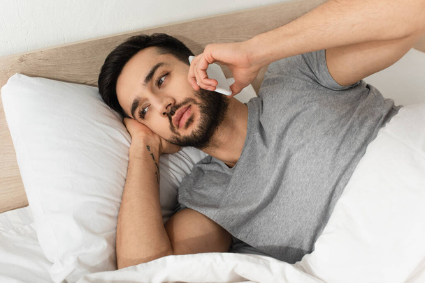 Bearded man talking on mobile phone while lying on bed  - Фото, зображення
