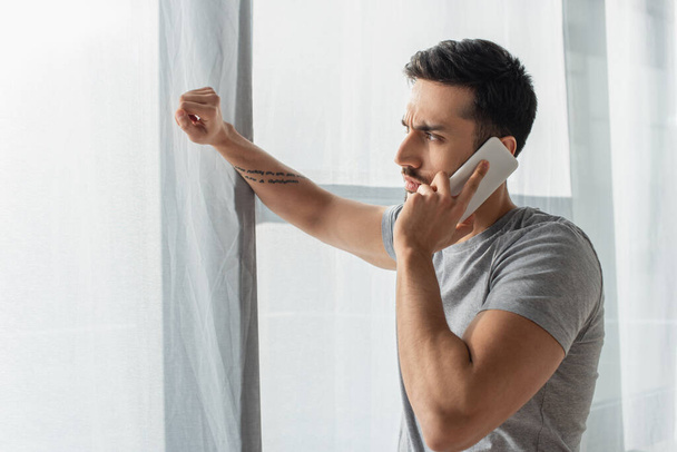 Side view of concentrated man talking on mobile phone near window  - 写真・画像