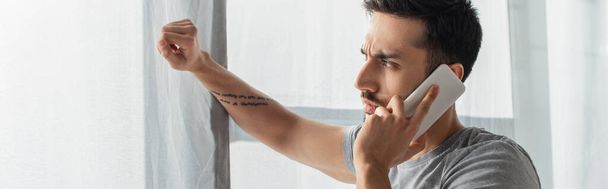 Vue latérale du jeune homme parlant sur smartphone près de la fenêtre, bannière  - Photo, image
