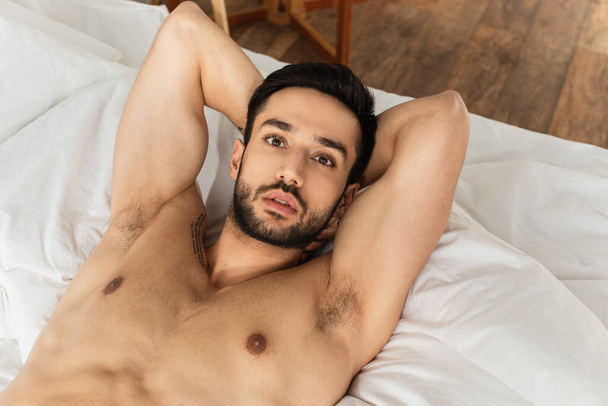 Top view of shirtless and bearded man looking at camera on bed  - Fotografie, Obrázek