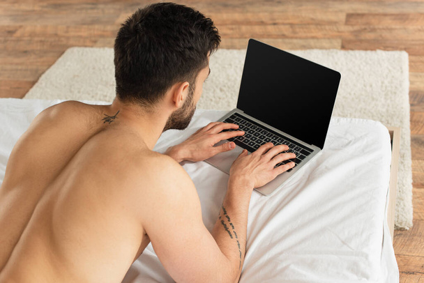 Pohled shora na muže bez trička používajícího notebook s prázdnou obrazovkou na posteli  - Fotografie, Obrázek