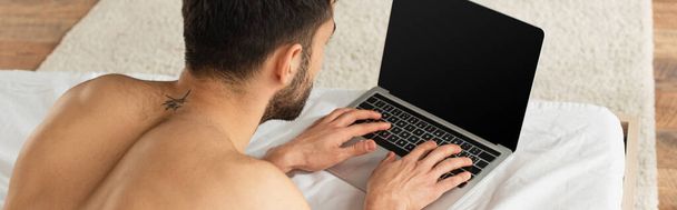 Vue arrière du pigiste torse nu à l'aide d'un ordinateur portable avec écran blanc sur le lit, bannière  - Photo, image