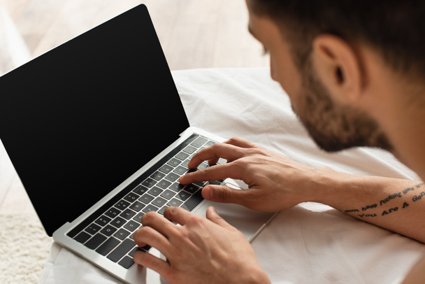 Bulanık adam dizüstü bilgisayar kullanıyor ve beyaz yatak örtüsünde boş ekran var.  - Fotoğraf, Görsel