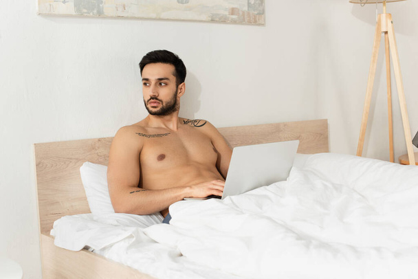 Teletrabajo muscular usando portátil mientras está sentado en la cama por la mañana  - Foto, imagen