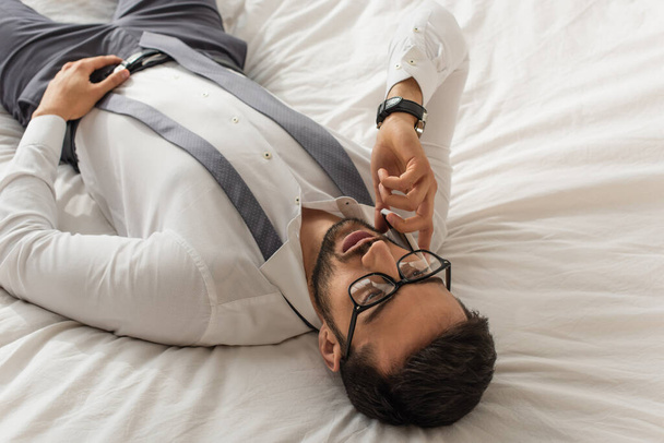 Korkea kulma näkymä liikemies muodollinen kulumista puhuu matkapuhelin sängyssä  - Valokuva, kuva