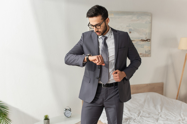 Businessman in eyeglasses looking at wristwatch in bedroom  - Zdjęcie, obraz