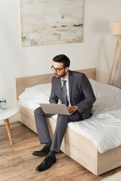 Young businessman using laptop while sitting on bed  - 写真・画像