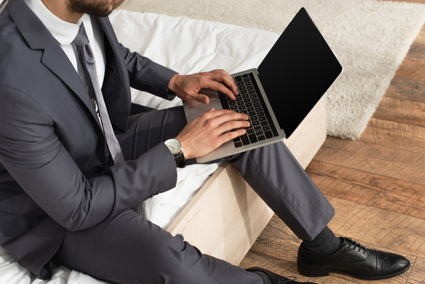 Vista cortada de empresário de terno usando laptop com tela em branco na cama  - Foto, Imagem