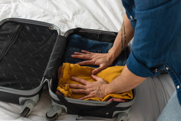 Cropped view of man pressing clothes in suitcase on bed  - Foto, Imagen