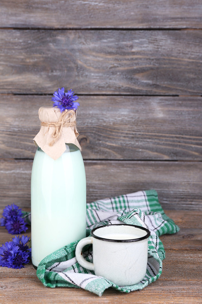 Bottle and cup of milk with cornflowers on wooden background - Photo, image